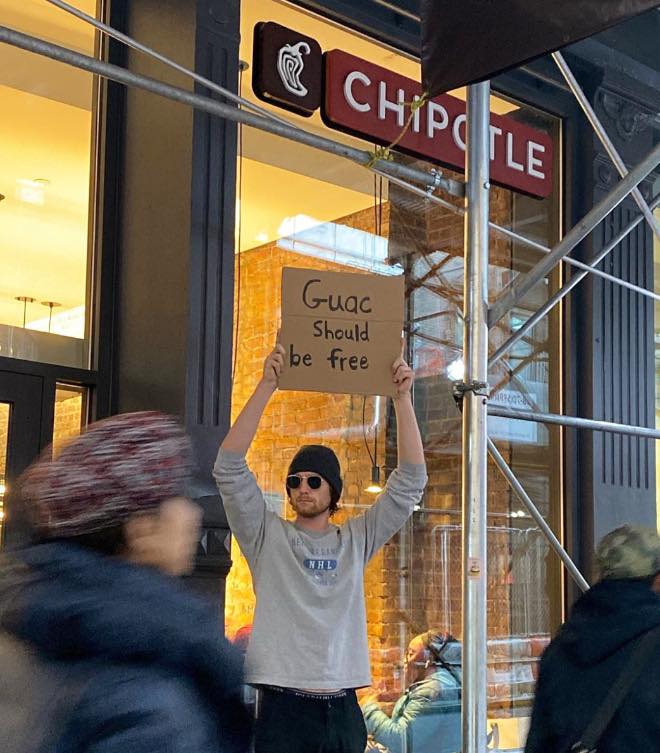 This meme features a person holding a sign outside a Chipotle restaurant, where a line of people are waiting to get in. The sign reads "Guac should be free" and is a playful reference to the popular Chipotle menu item. The sign is a humorous way to express the frustration of waiting in line and the desire to have free guacamole.